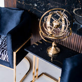 Gold armillary sphere on a black marble table with a blue chair and zebra-patterned cushion in the background.