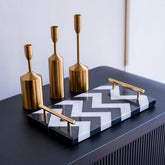 Decorative set with gold candle holders and a black and white zigzag tray on a dark surface.