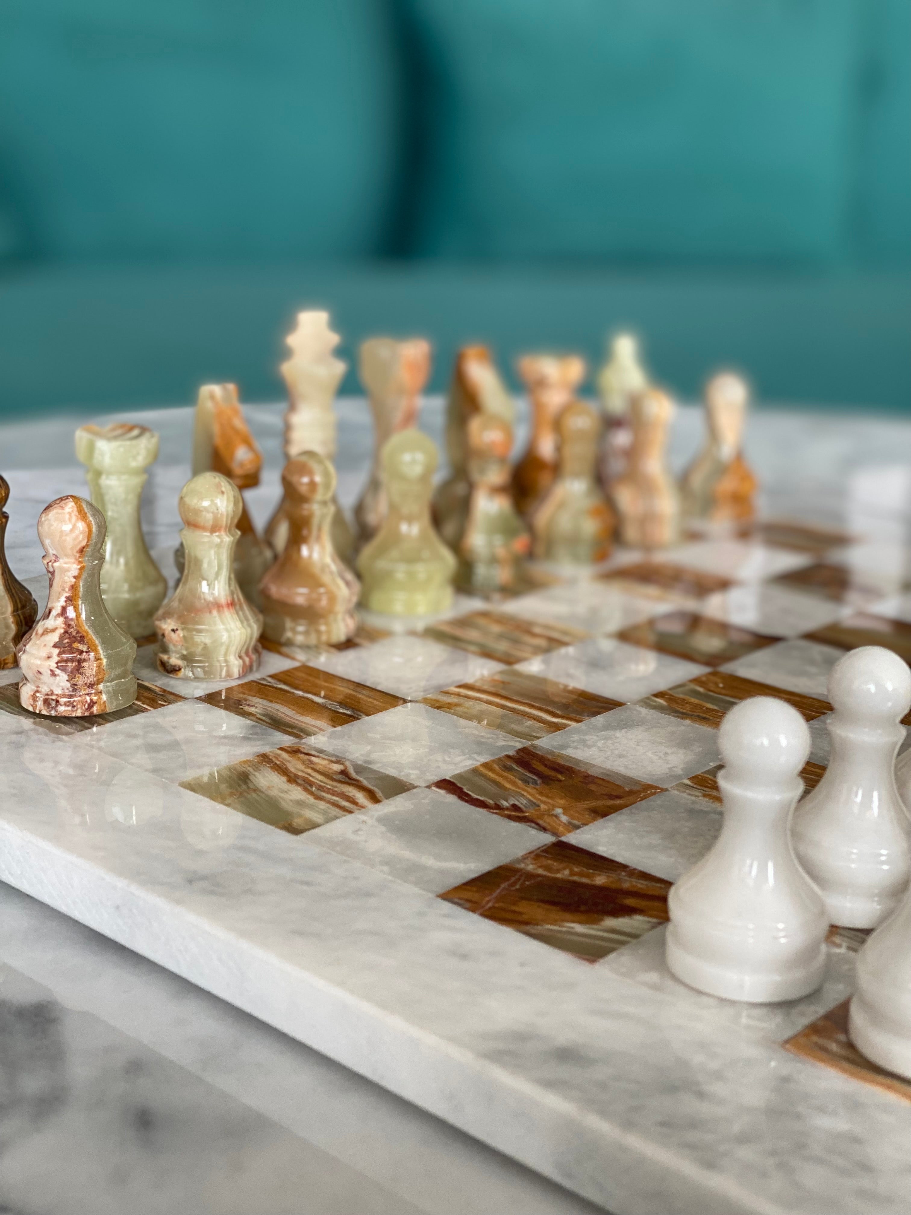 Marble chessboard with assorted chess pieces on a teal sofa background