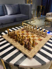 Decorative chessboard with wooden pieces on a black and white striped surface, with a gray sofa and gold mirror in the background.