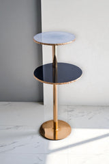 Two-tiered side table with gold base and black and blue glass shelves against a gray wall.