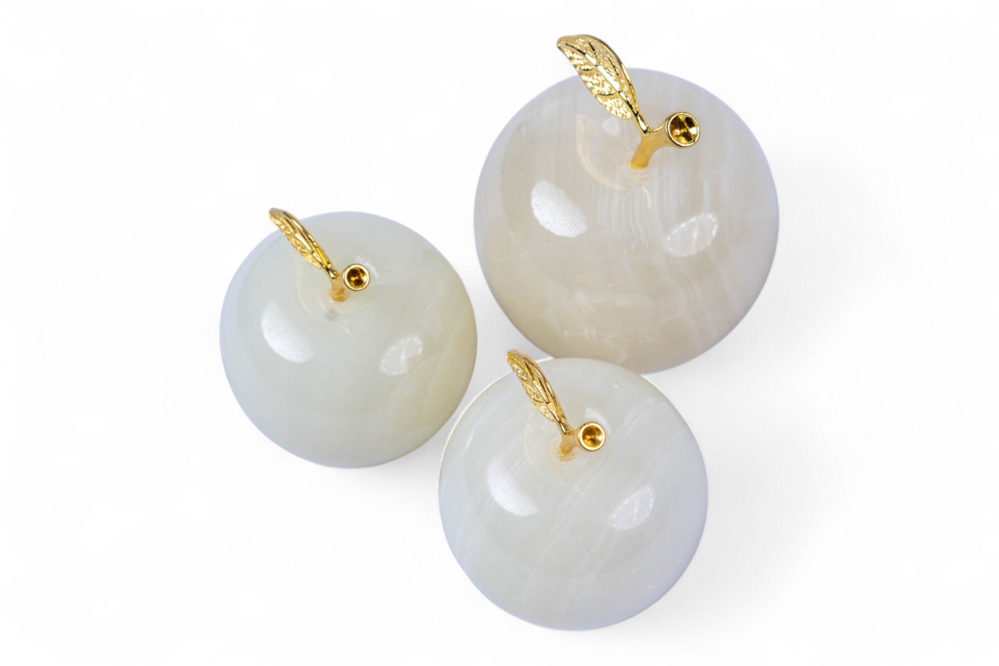 Three white spherical objects with gold hooks on a white background