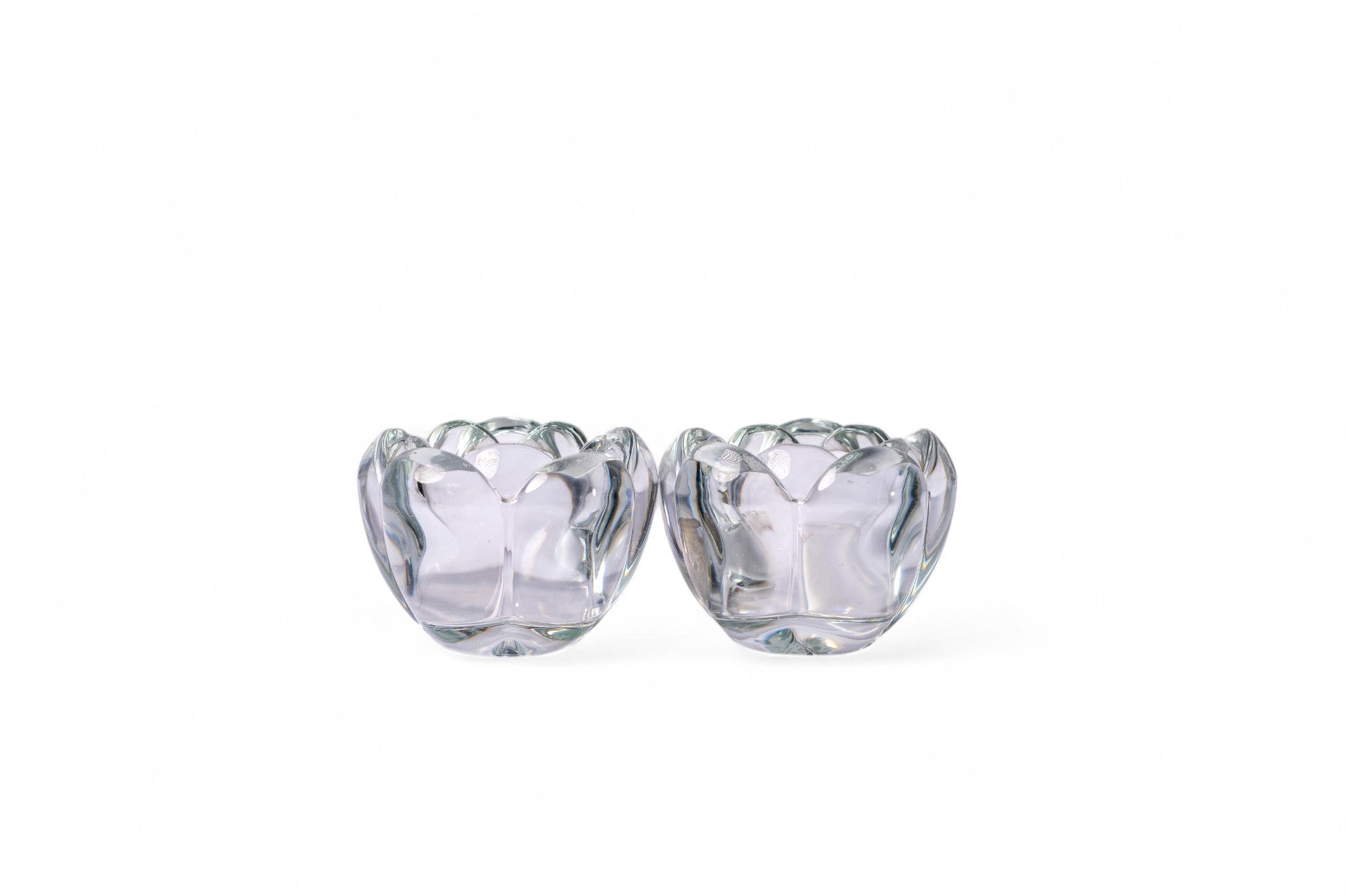 Two clear glass lotus-shaped candle holders on a white background