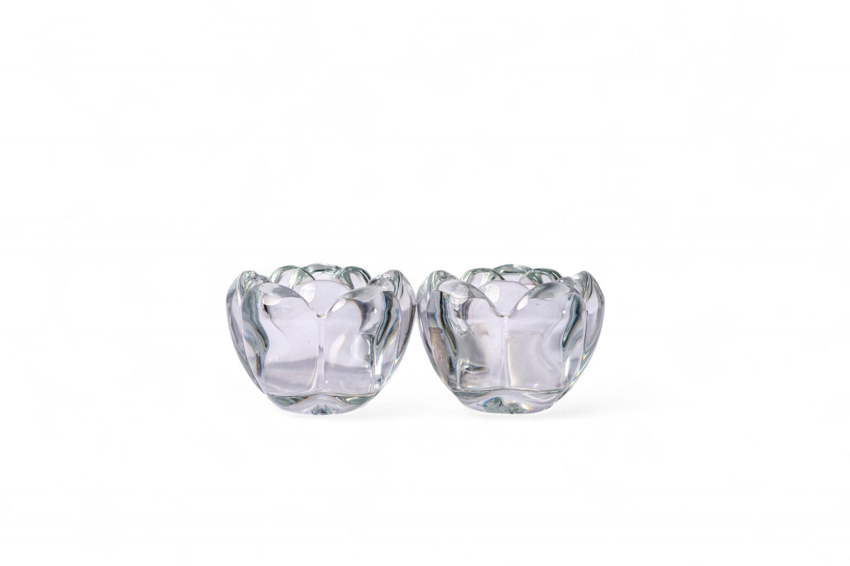 Two clear glass lotus-shaped candle holders on a white background