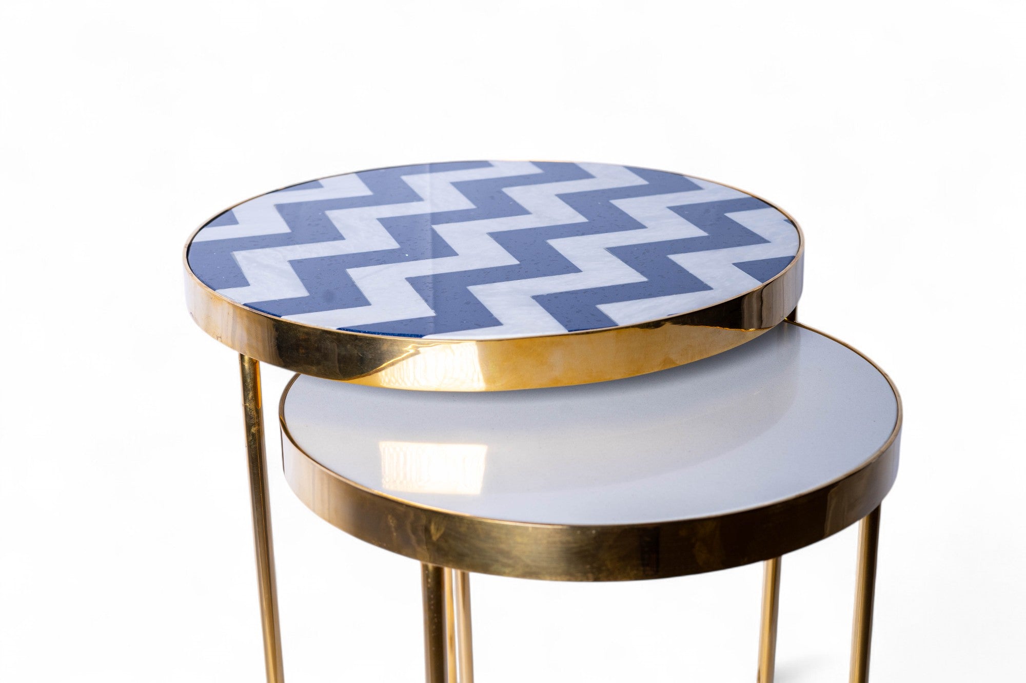Set of two round tables with gold legs and patterned tops on a white background