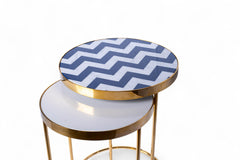 Round side table with gold frame and blue and white zigzag patterned top on a white background
