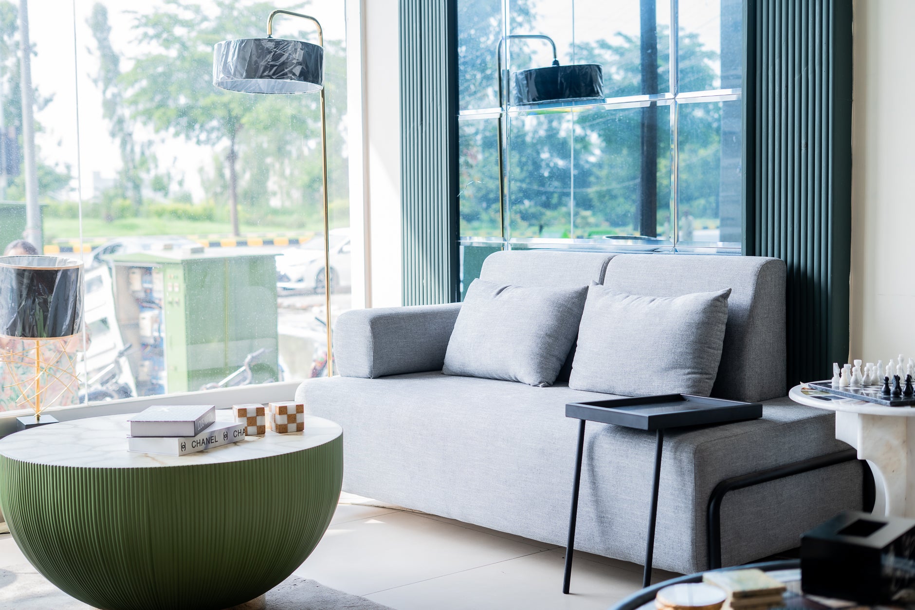Modern living room with a gray sofa, round green coffee table, and large windows.