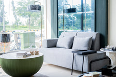 Modern living room with a gray sofa, round green coffee table, and large windows.