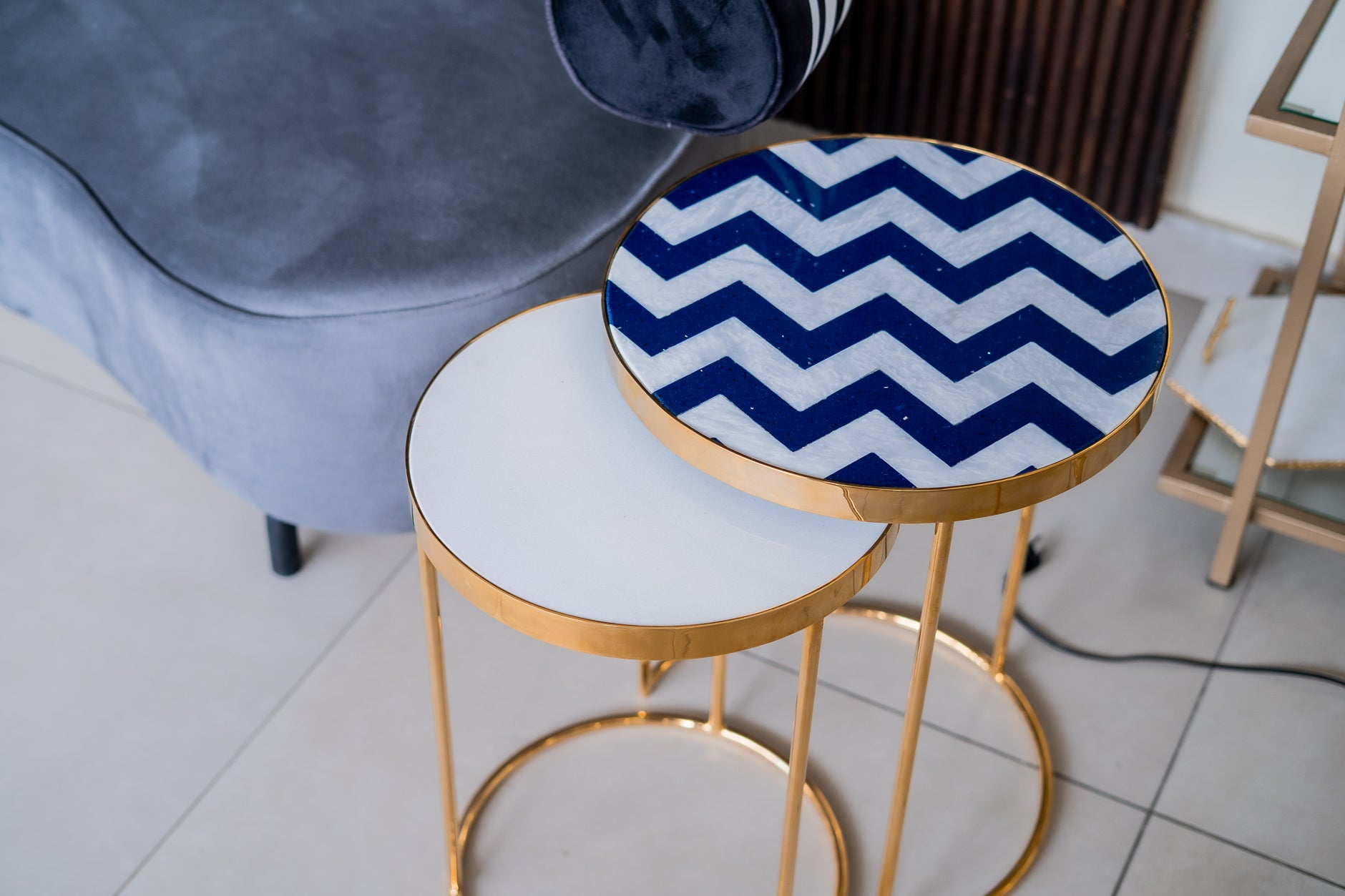 Round table with a blue and white zigzag pattern on a gold frame, next to a gray chair.
