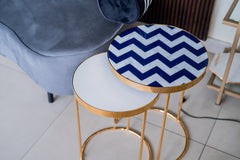 Round table with a blue and white zigzag pattern on a gold frame, next to a gray chair.