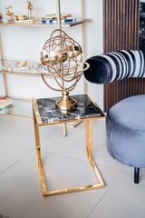 Decorative gold armillary sphere on a marble side table with a chair and shelf in the background.