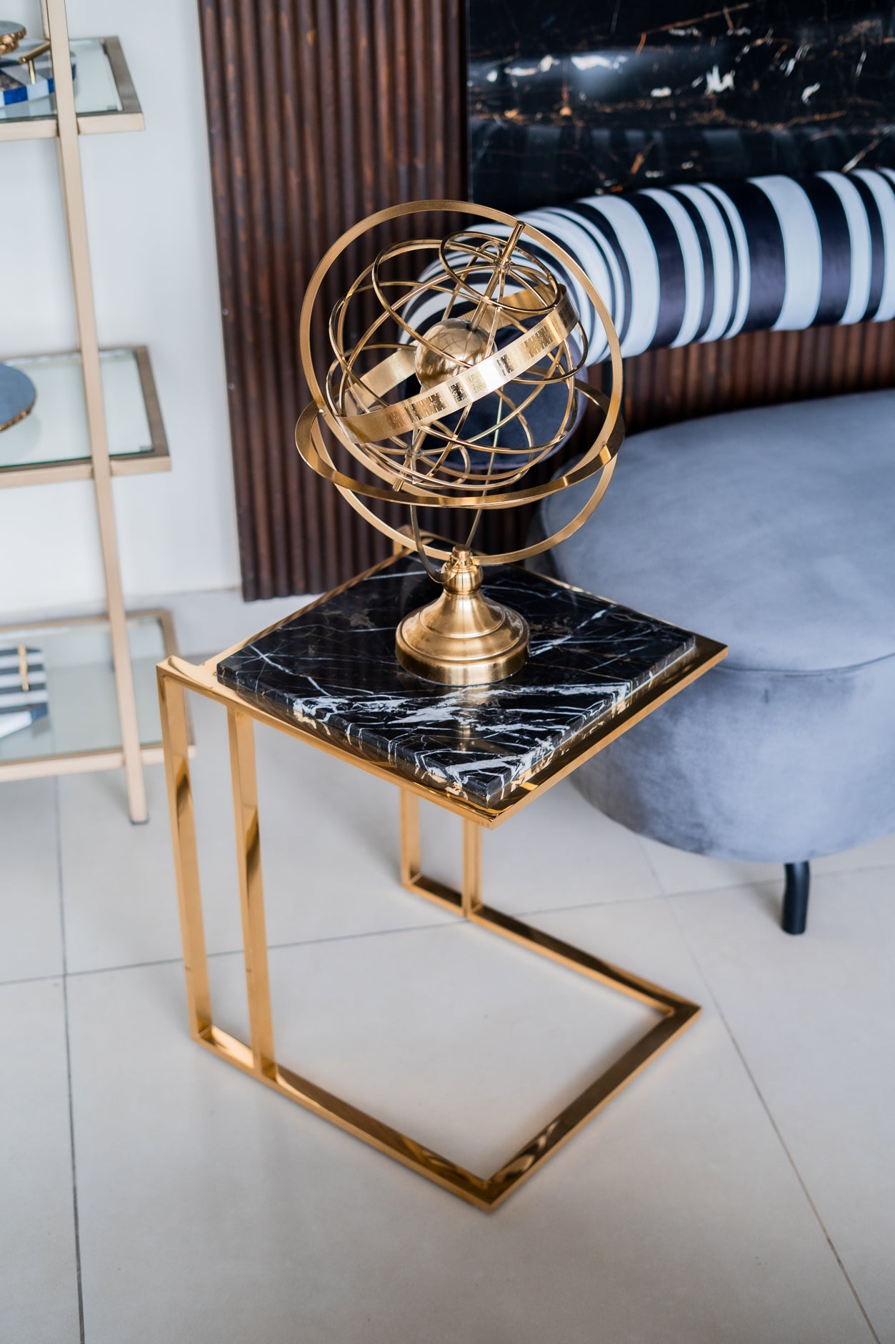 Decorative gold sphere on a black marble side table with a striped cushion in the background.