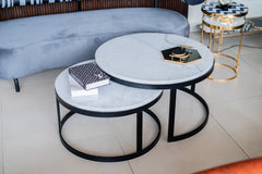 Set of round marble coffee tables with black metal frames in a living room setting.