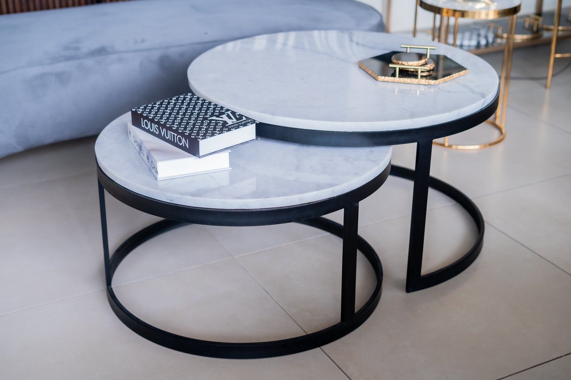 Two round marble coffee tables with black metal frames on a tiled floor.