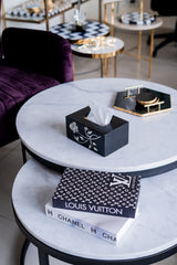 Round marble coffee table with a tissue box, books, and decorative items in a stylish interior setting.
