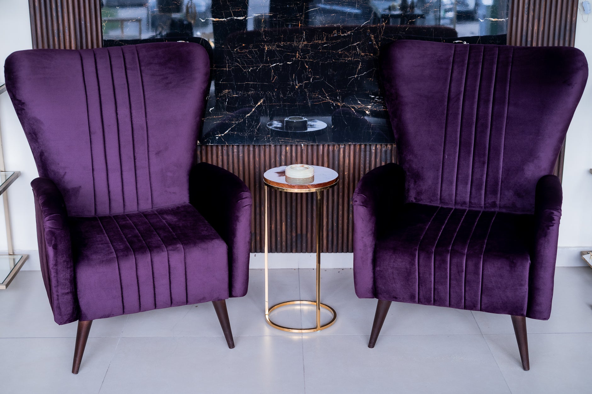 Two purple armchairs with a small round table in a room with marble wall.