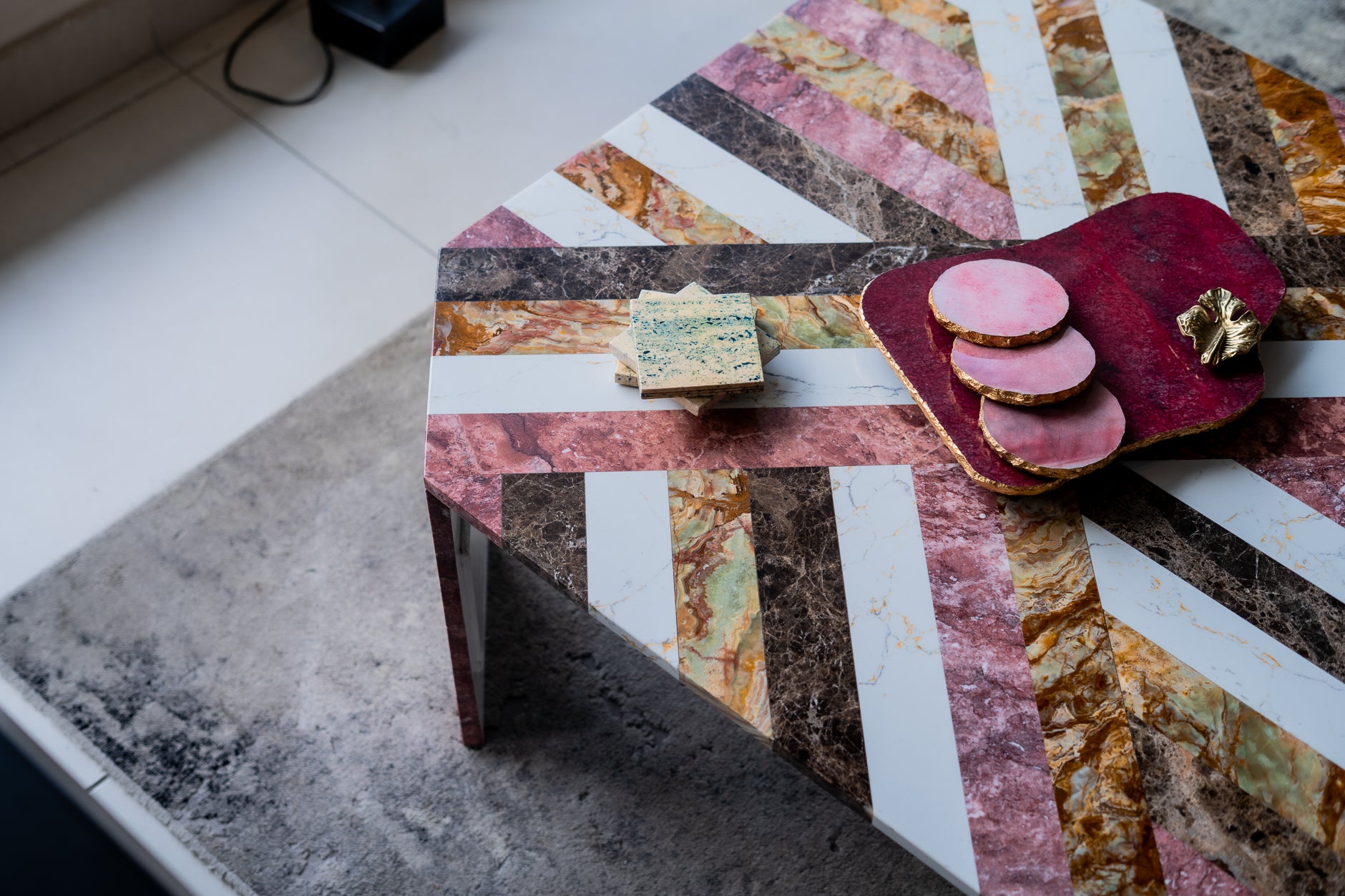Colorful geometric-patterned table with a small stack of books and a pink decorative item on a textured surface.