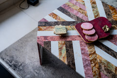 Colorful geometric-patterned table with a small stack of books and a pink decorative item on a textured surface.