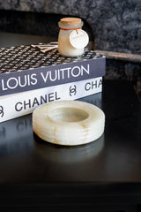 Small jar candle on top of a stack of fashion magazines with visible brand names.