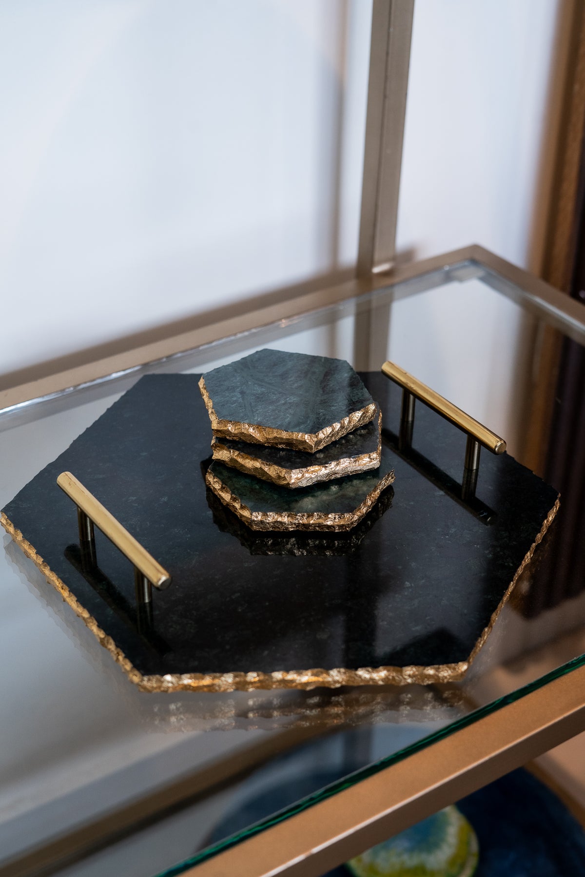Set of black stone coasters with gold edges on a glass shelf.