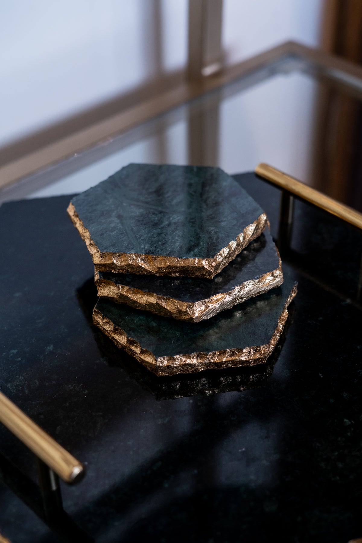 Set of hexagonal black stone coasters with gold edges on a dark surface.