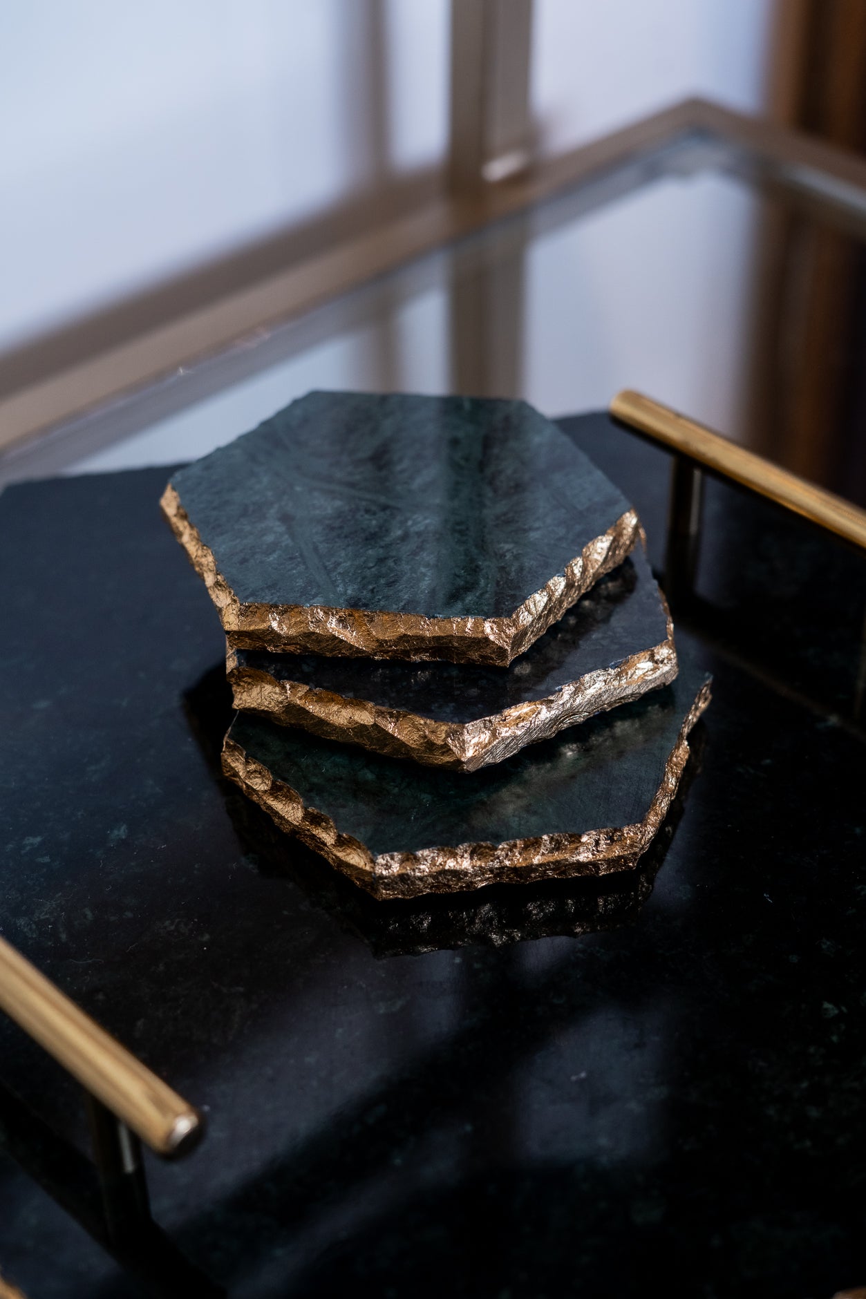Set of hexagonal black stone coasters with gold edges on a dark surface.