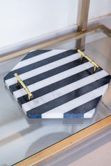 Hexagonal marble tray with black and white stripes and gold handles on a glass surface.