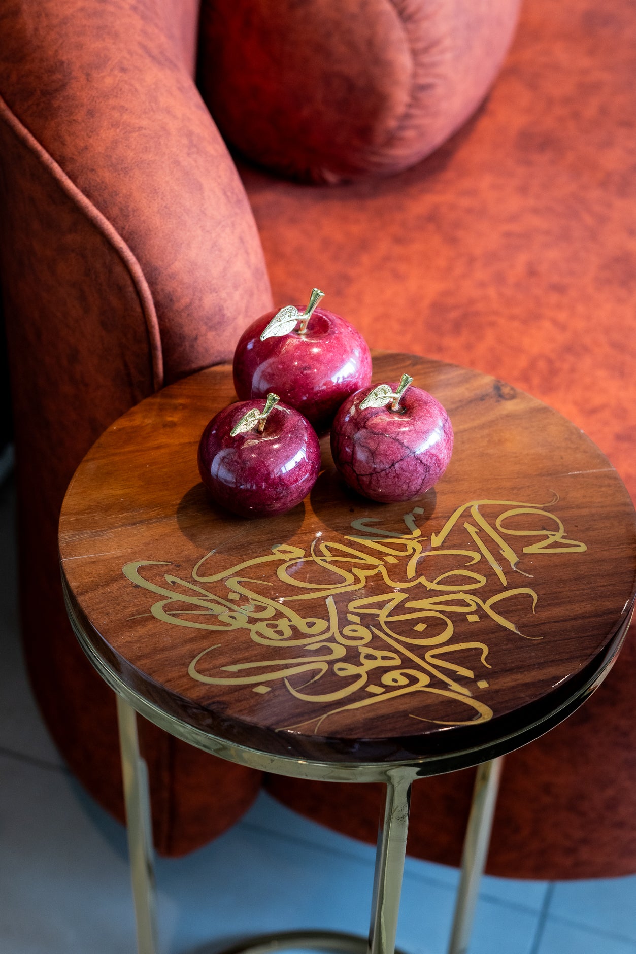 Wooden stool with gold calligraphy and three red apples on a red couch background