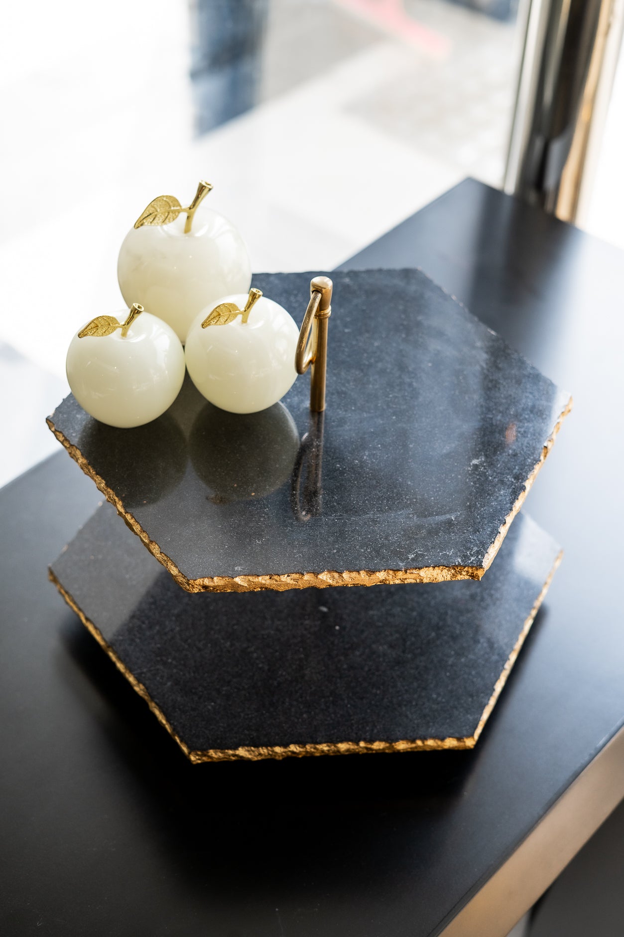 Three white apples with gold accents on a black hexagonal stone stand.