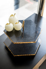 Three white apples with gold accents on a black hexagonal stone stand.