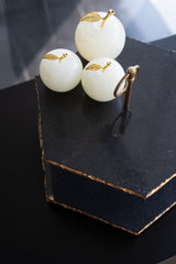 Three white spherical desserts with gold leaf decorations on a black stand.