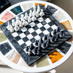 Chessboard with black and white pieces on a round table with a colorful surface.