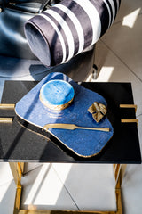 Blue ceramic dish with a gold leaf on a black tray, with a striped hat in the background.