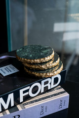 Stack of green marble coasters on a book titled 'Tom Ford' with a blurred background