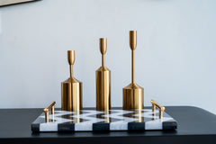 Set of gold candle holders on a black and white patterned tray against a light gray wall.