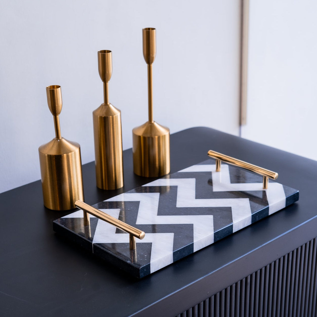 Decorative set with gold candle holders and a black and white zigzag tray on a dark surface.