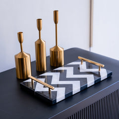 Decorative set with gold candle holders and a black and white zigzag tray on a dark surface.