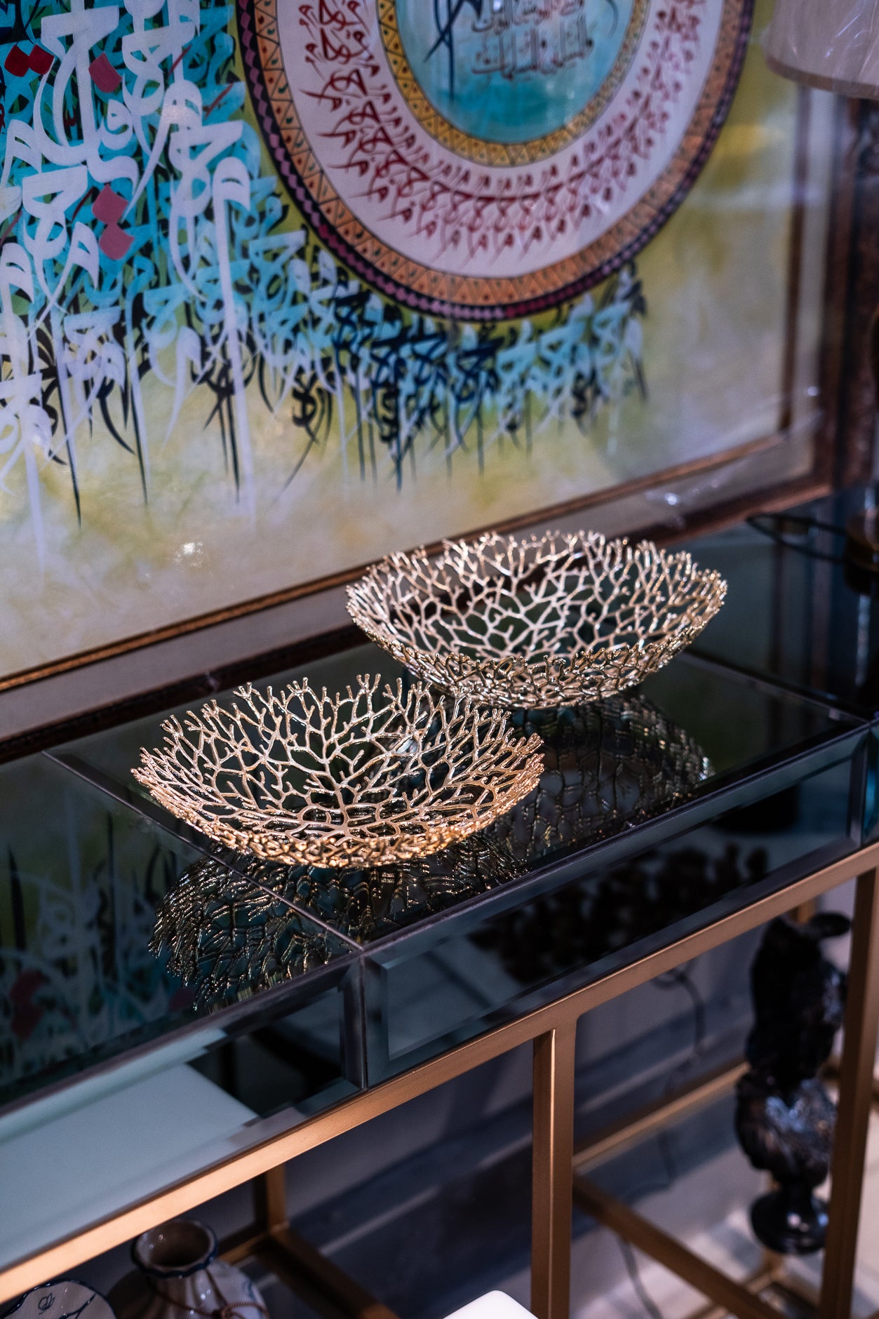 Decorative metal bowls on a reflective surface with a colorful abstract painting in the background
