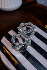 Two clear glass candle holders on a black and white striped surface.