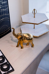 Gold elephant figurine on a desk with a two-tiered serving tray in the background.
