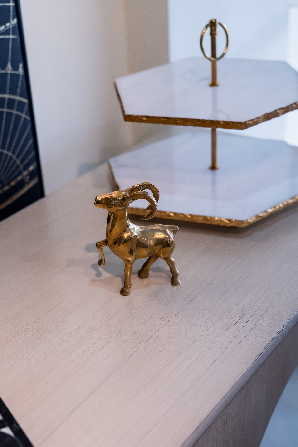 Gold ram figurine on a light wooden surface with a white hexagonal tray in the background.