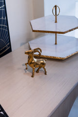 Gold ram figurine on a light wooden surface with a white hexagonal tray in the background.