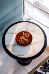Round marble table with a wooden coaster featuring a scorpion design on a marble floor.