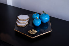 Blue decorative fruits on a black and gold hexagonal plate with a white background